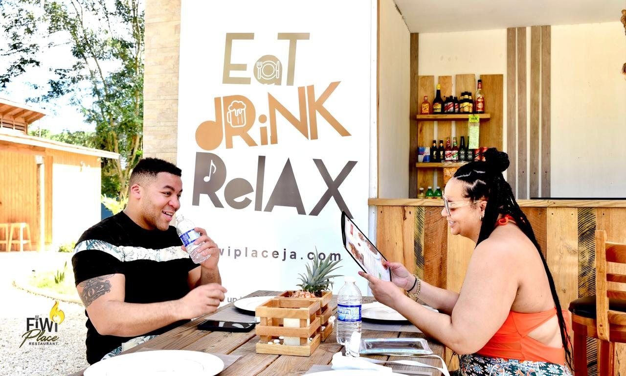Guests relaxing at a table by the Eat Drink Relax sign at FiWi Place